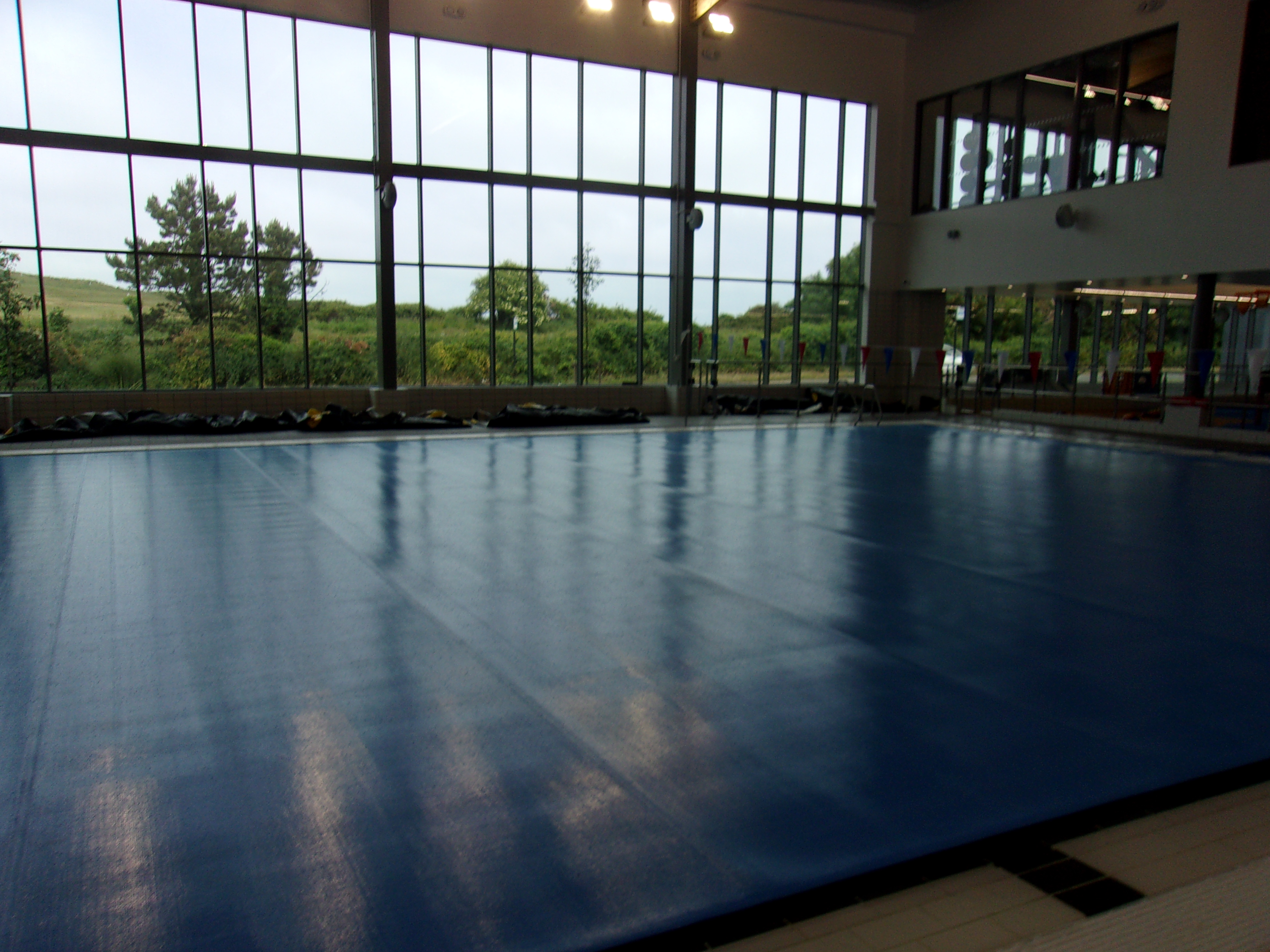 Image of the pool cover over the Reef Leisure Centre swimming pool at sunset. Large glass walls look out to greenery.